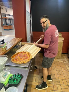 Owner Jason Natoli loading a pizza into the oven with a peel