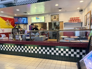Inside Trattoria Natoli — checkered tile counter, Sicilian flag and menu boards